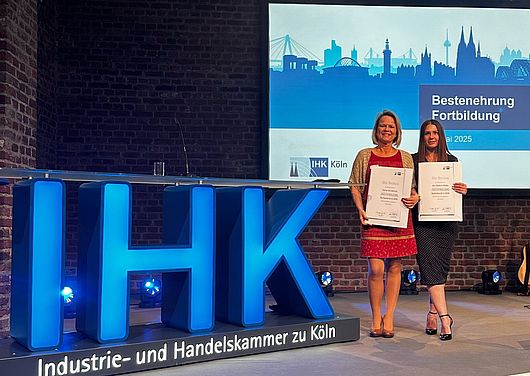 Carina Wunderlich und Ann-Kathrin Müller halten die Auszeichnung der IHK Köln in den Händen.